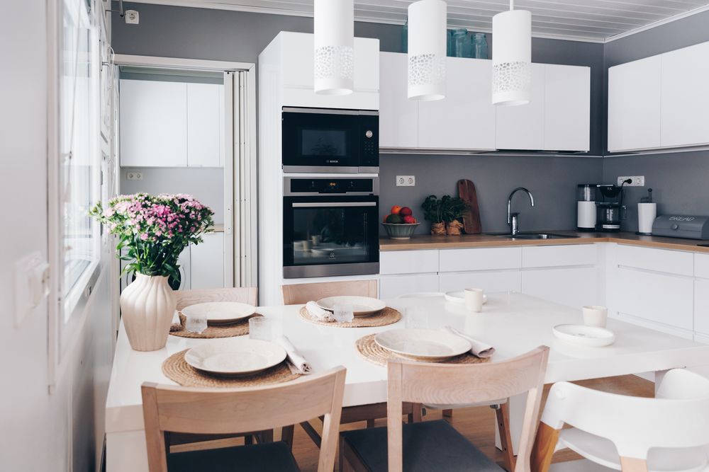 Modern white kitchen with light wood dining table, white chairs, and minimalist decor in an open concept space.