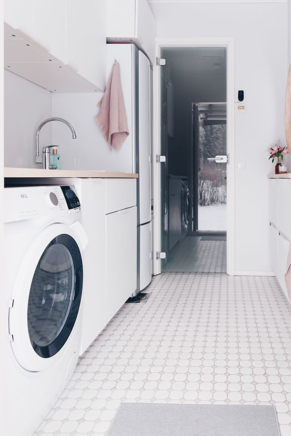 Modern minimalist laundry room with white washing machine, stainless steel fridge, and tiled floor in soft neutral tones.