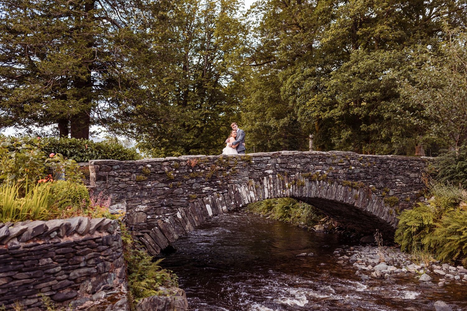 Natural wedding photography at Lodore Falls Hotel - bride and groom embrace on top of the stone bridge