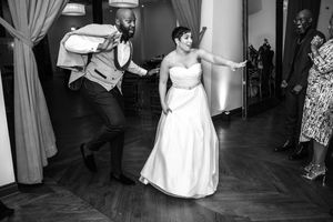 Wedding guests dance together in a reception hall with elegant curtains and lighting.