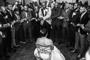 A black and white photo shows a crowd gathered in a circle watching two people dancing at what appears to be a wedding reception.