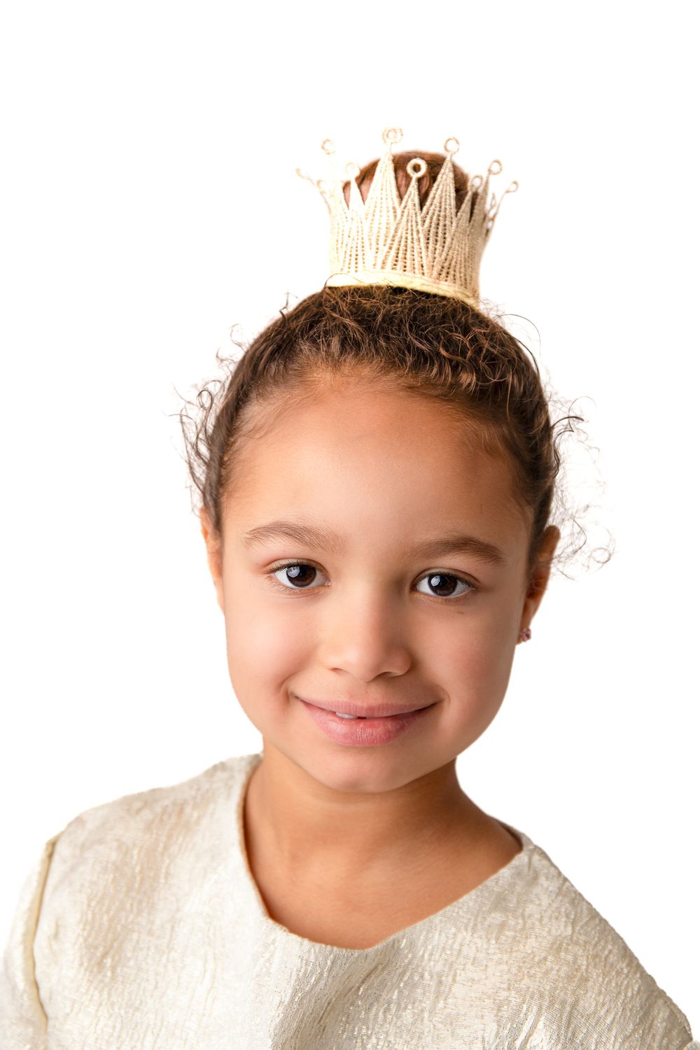 Young girl wearing a small gold crown on her head, smiling against a white background.
