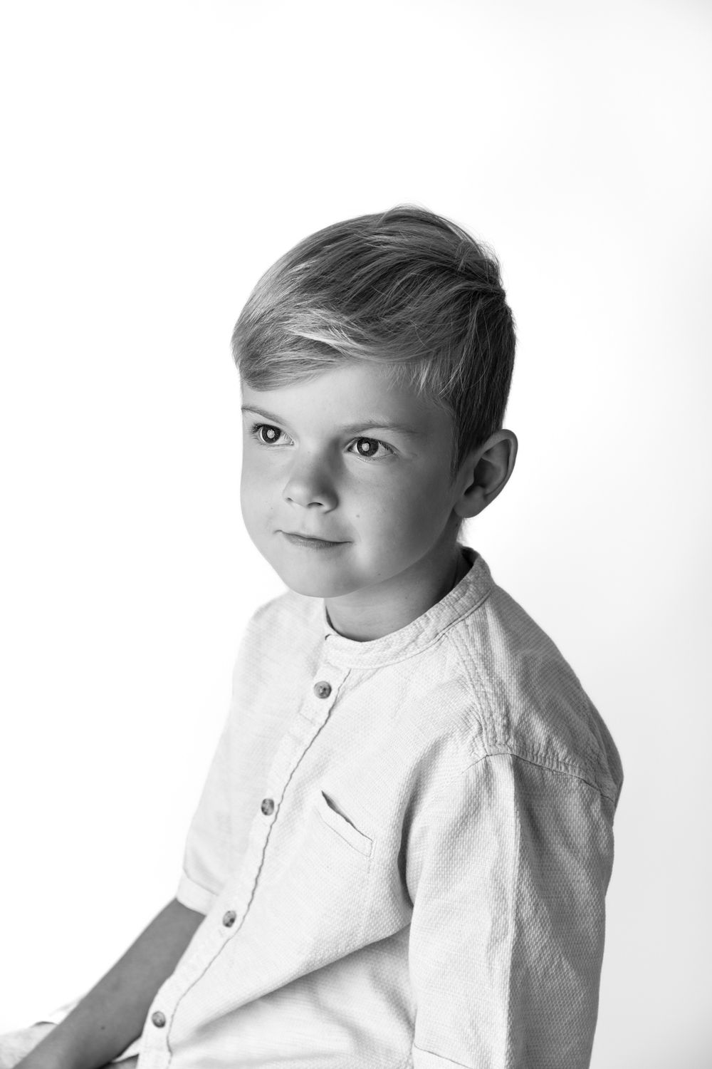 Black and white portrait of a young boy in a light button-up shirt, looking at the camera with a slight smile.