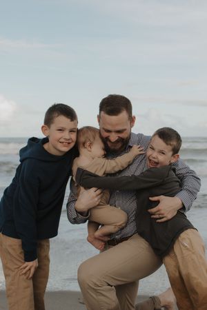 Family shares joyful moments playing and embracing together on a cloudy beach.