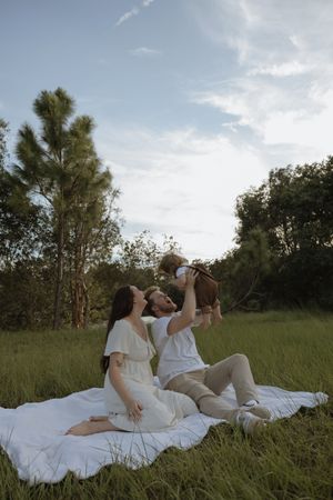 A family lounges together on a white blanket in a grassy field during golden hour.