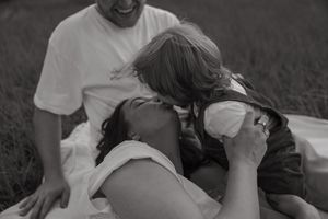 A tender black and white moment captured between people lying on a blanket outdoors in a grassy field.