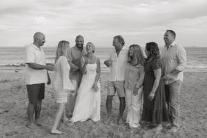A group of people in light colored clothing gather on a beach during what appears to be a casual celebration or event.
