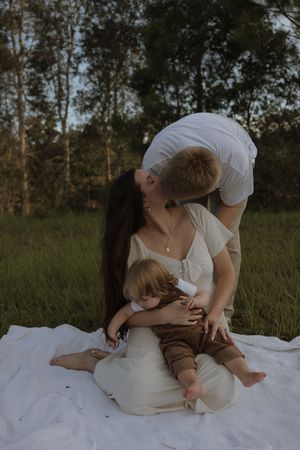 A tender family moment captured on a white blanket in a sunlit meadow.