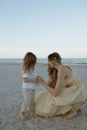 A tender moment shared between two people in light flowy clothing on a peaceful sandy beach at dusk.