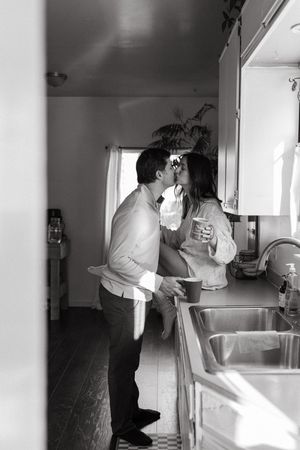 Black and white photos showing intimate kitchen moments between a couple in a sunlit home interior.