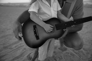 Monochrome close-up shots of hands playing acoustic guitars on a sandy beach.