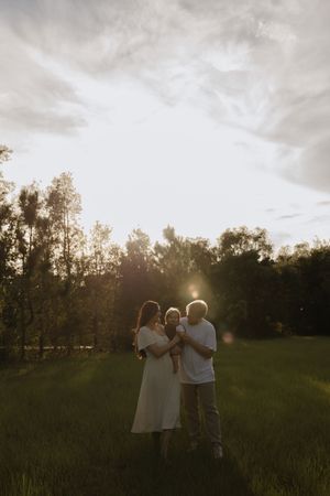A couple embraces in a serene field during sunset with trees silhouetted in the background.