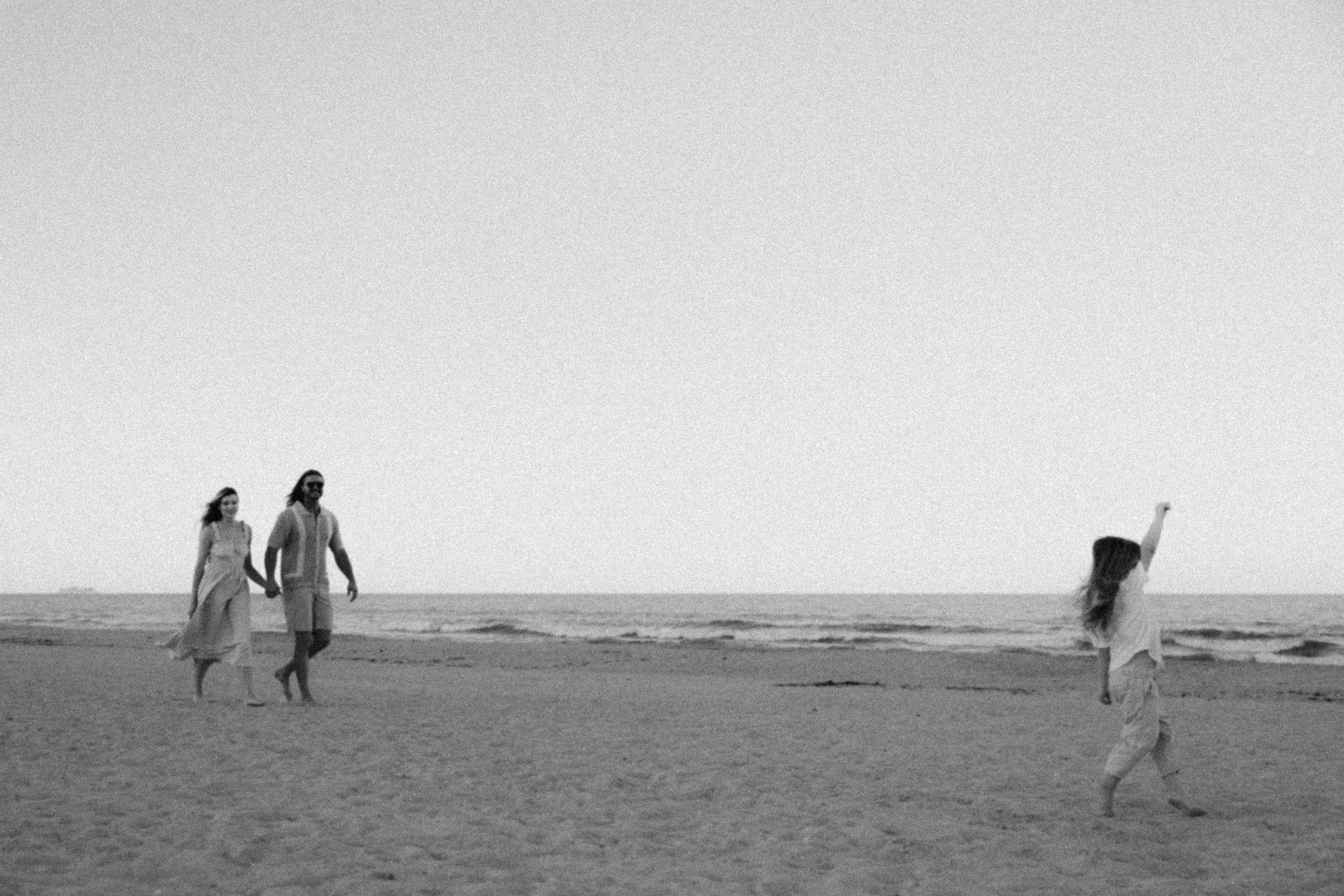 A series of black and white photographs showing figures walking along a misty beach at sunset.
