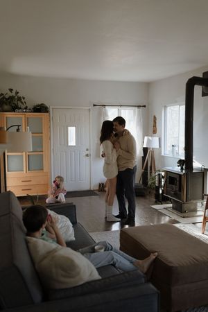 A cozy living room scene with people relaxing on a sofa while others share an intimate moment by the doorway.