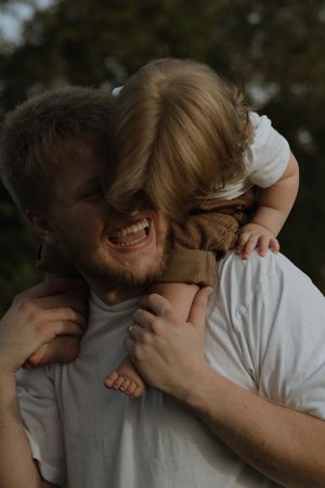 A joyful moment captured between a bearded man in a white t-shirt and a small child playing together outdoors.