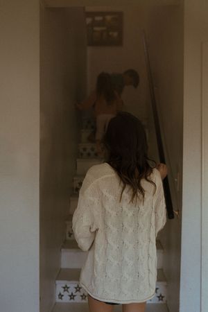 A person in a white knit sweater looking at their reflection in a bathroom mirror.