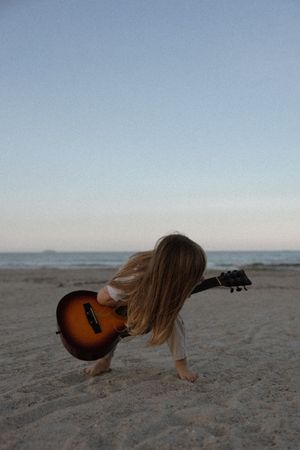 A sequence showing an acoustic guitar lying on sandy beach at different angles during sunset.