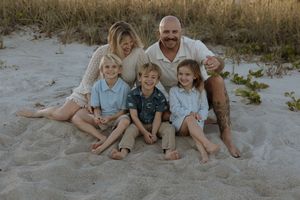 A family group lounges together on a sandy beach during a relaxed outdoor photo session at sunset.