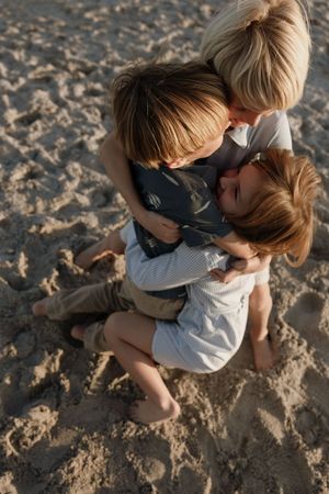 Intimate family moment captured from above showing a tender embrace on sandy beach at golden hour.