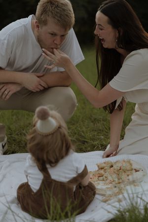 A couple having a picnic on a white blanket in the grass while sharing food together.