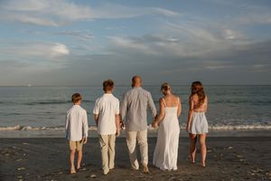 A group of people in white clothing stand together facing the ocean at sunset on a sandy beach.