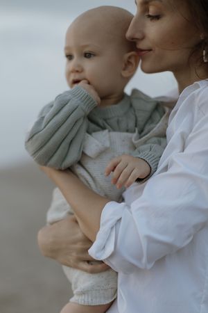 A tender moment between parent and baby wearing a mint green sweater against a soft gray background.