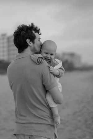 Black and white photos show tender moments between a parent and young child embracing on a beach.