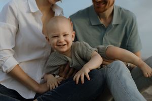A family sits together on a grey couch in a bright room while sharing joyful moments and laughter.