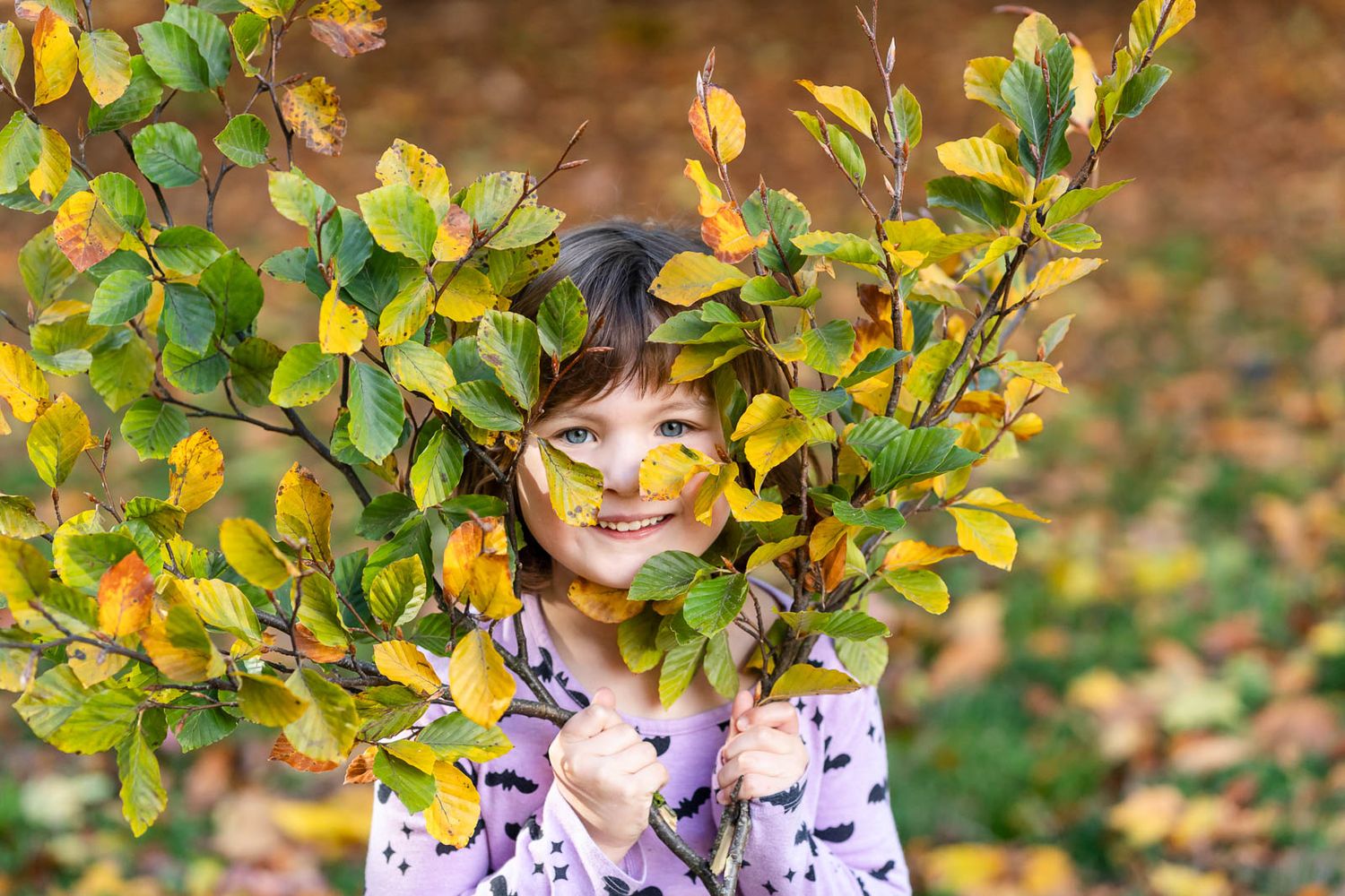 Girl smiling at the camera while framing her face with two tree branches.