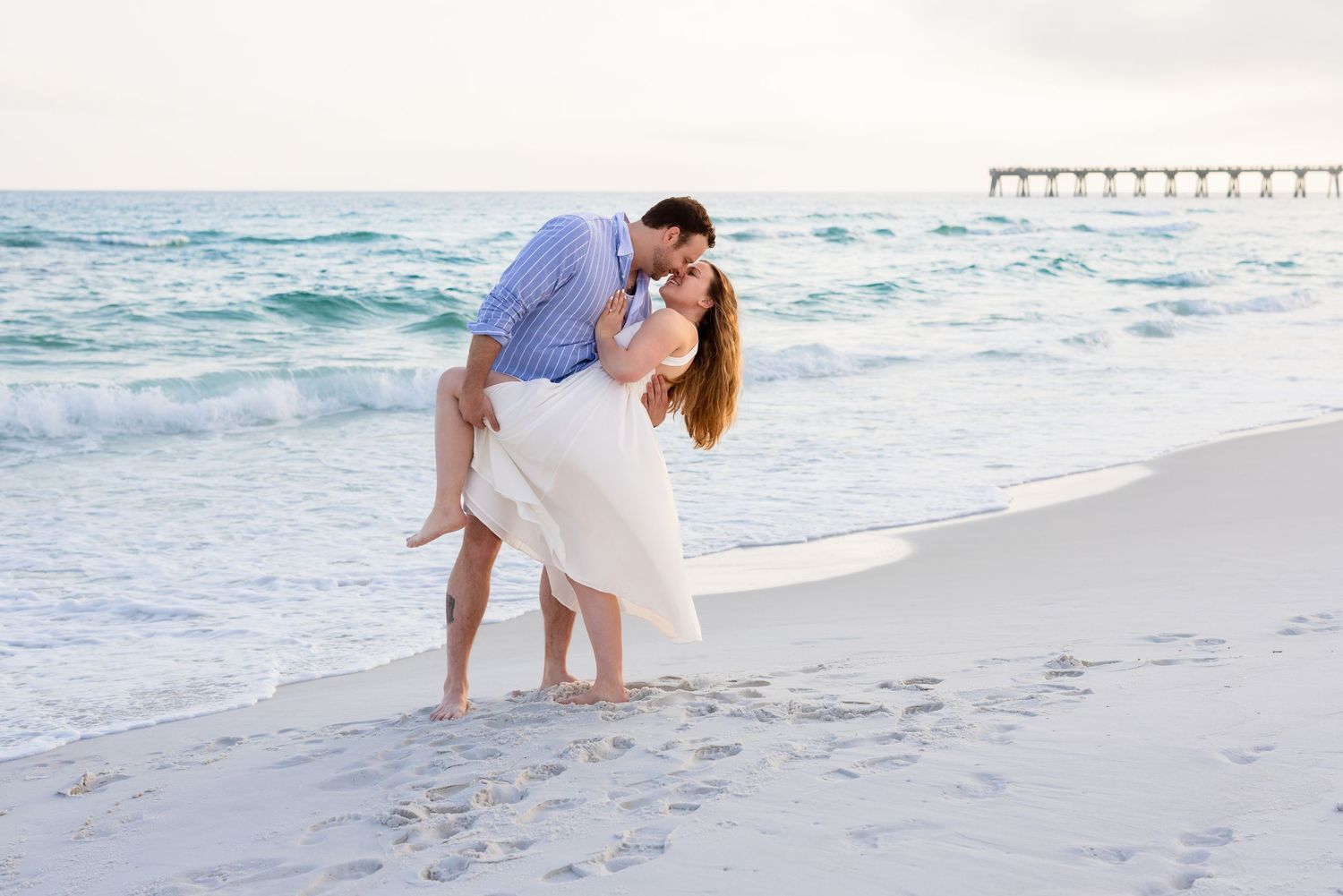 A romantic beach photoshoot at sunset with two people walking along the shoreline as waves crash nearby.