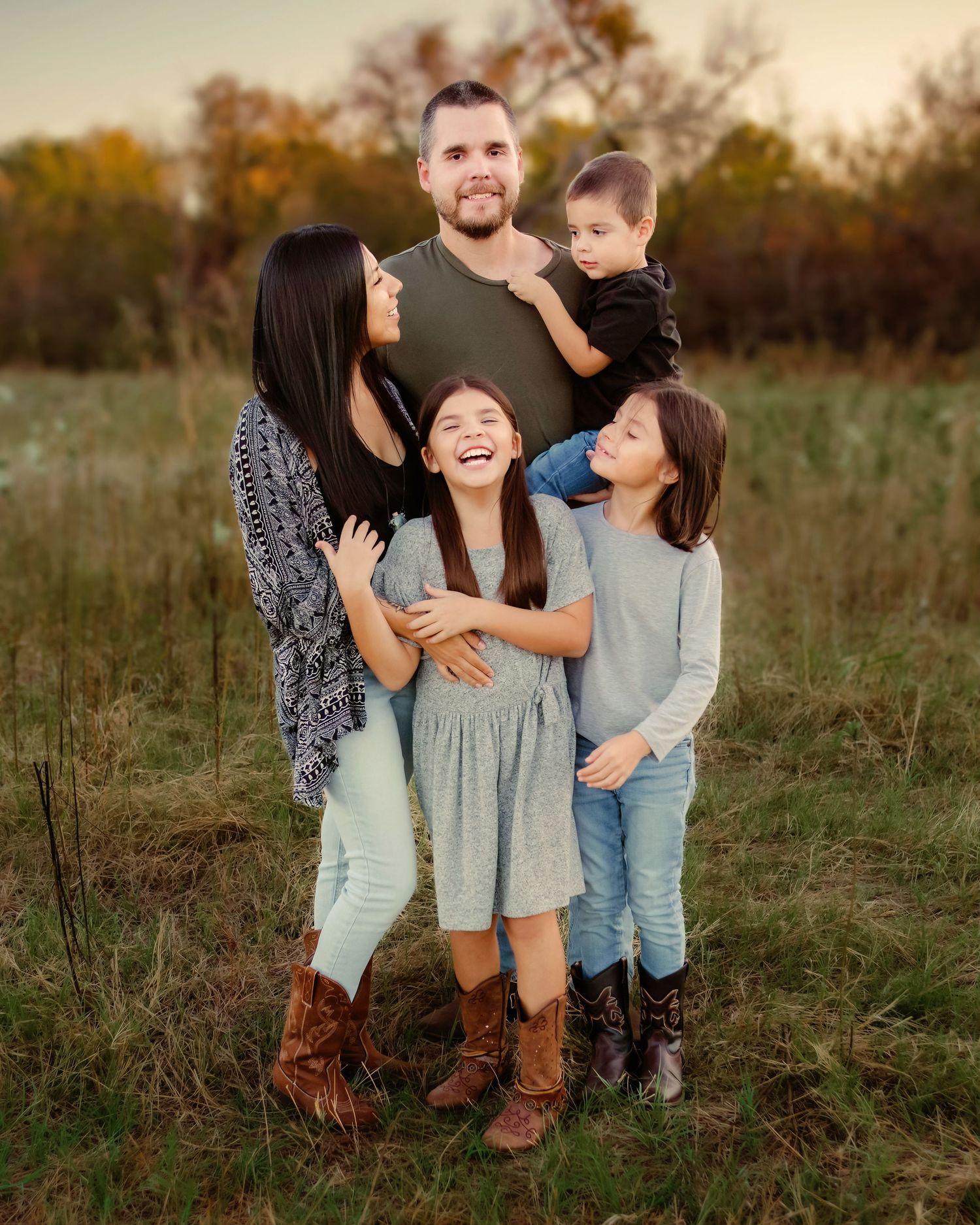 A joyful family laughs together while sitting in a grassy field during golden hour in Fort Worth, TX.