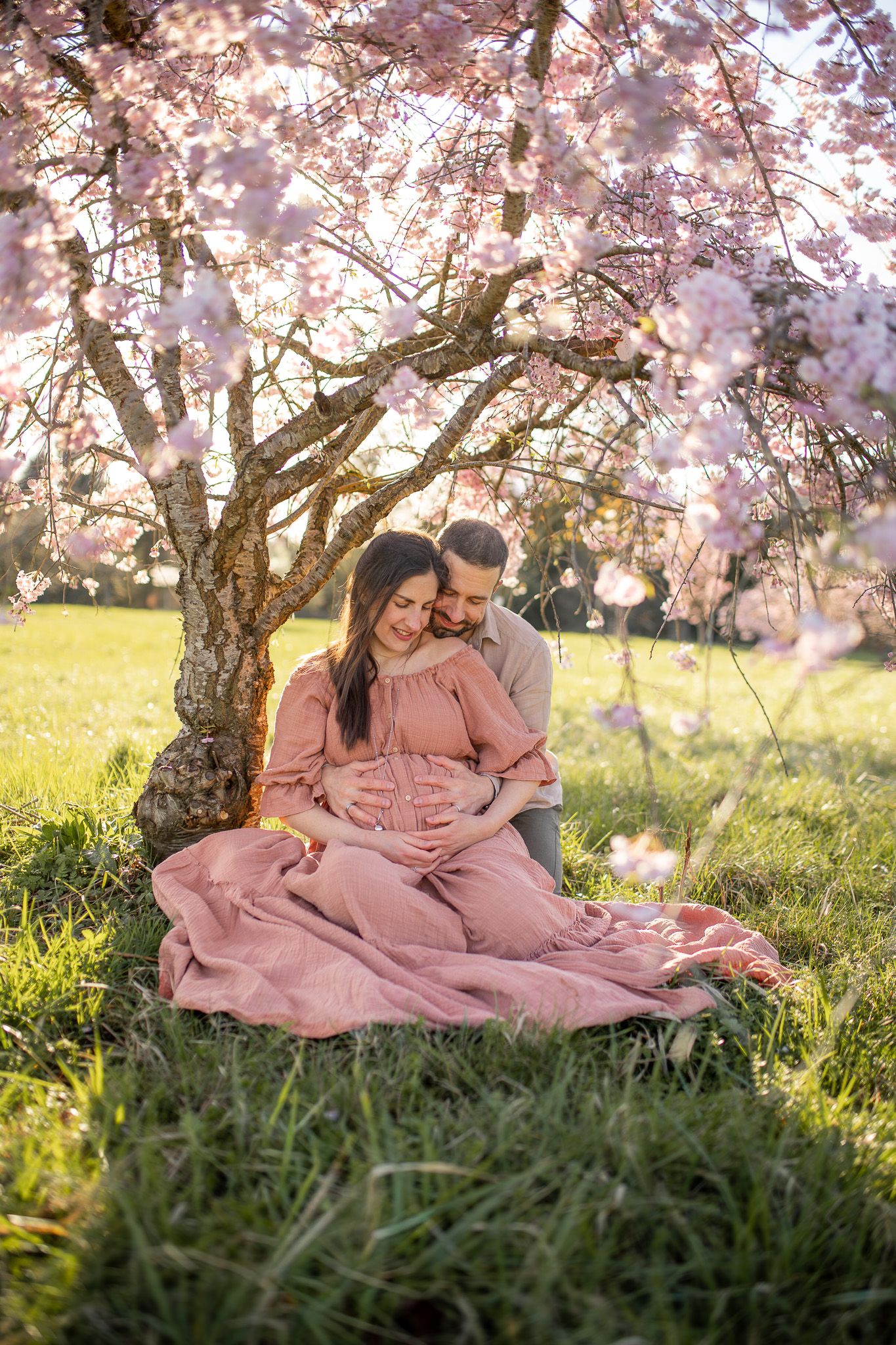 Couple lors d’une séance photo grossesse en extérieur sous un cerisier en fleurs, moment tendre et naturel