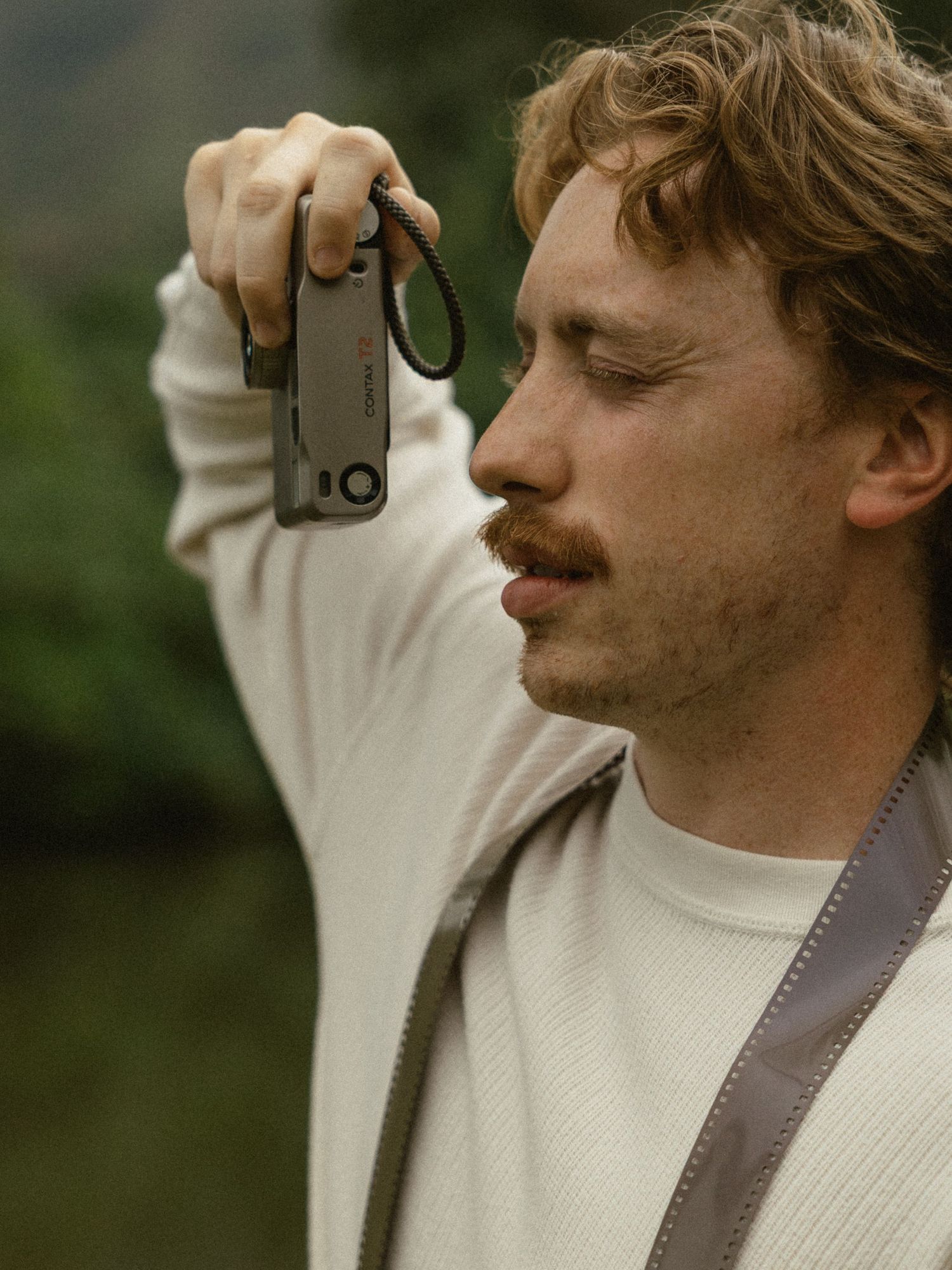 A photographer wearing dark clothing sits in tall grass while taking pictures with a vintage camera.