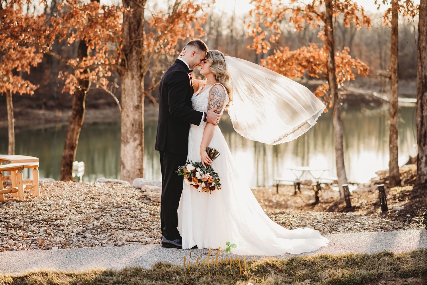 Bride and groom touch foreheads while groom hugs bride at the waist. Her vail is blowing behind her