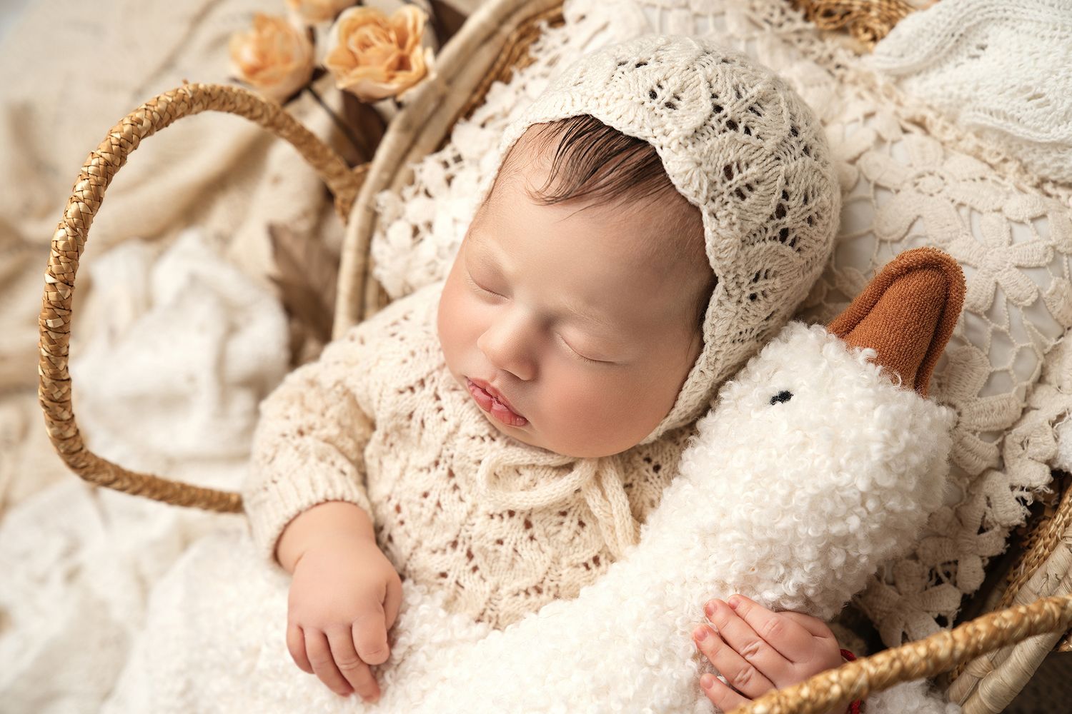 Two sleeping babies wrapped in soft pink blankets lie surrounded by delicate spring blossoms on white wooden flooring.