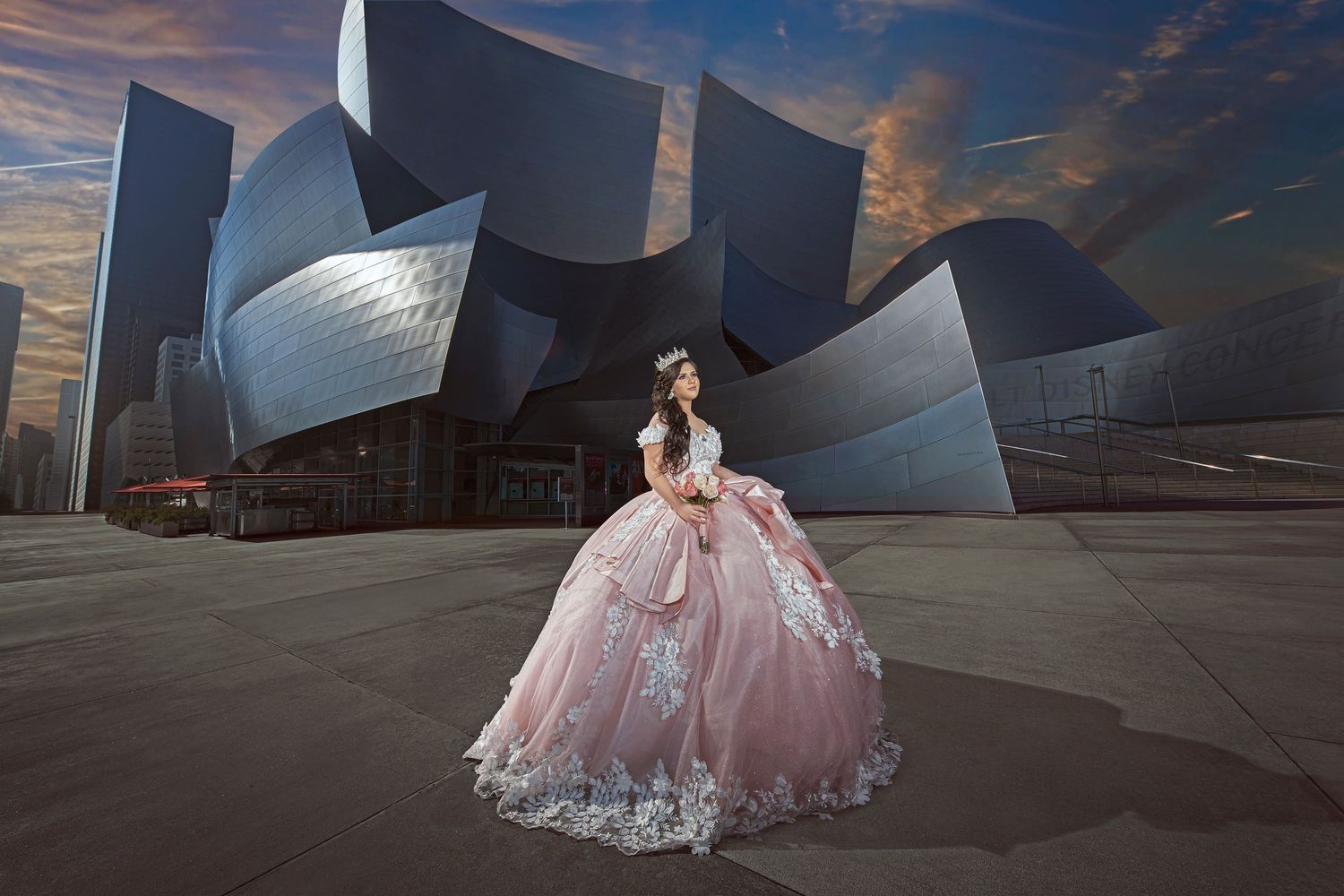 Young woman in pink quinceañera ball gown poses before Walt Disney Concert Hall at sunset in Los Angeles.