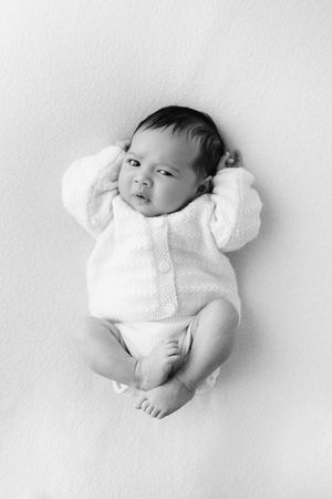 High-key portrait series of infant wearing white knit outfit against light background.