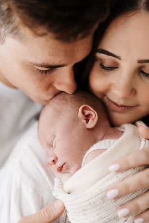 A serene newborn sleeping between parents who share an intimate moment.