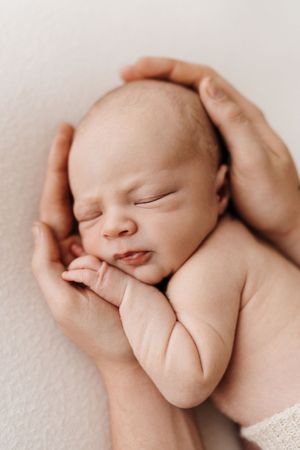 A peaceful sleeping newborn baby cradled gently in caring hands.