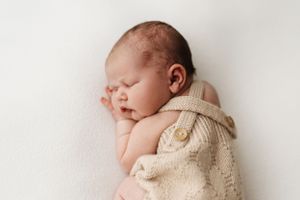 Peaceful newborn baby sleeping while wrapped in soft beige knit blanket.