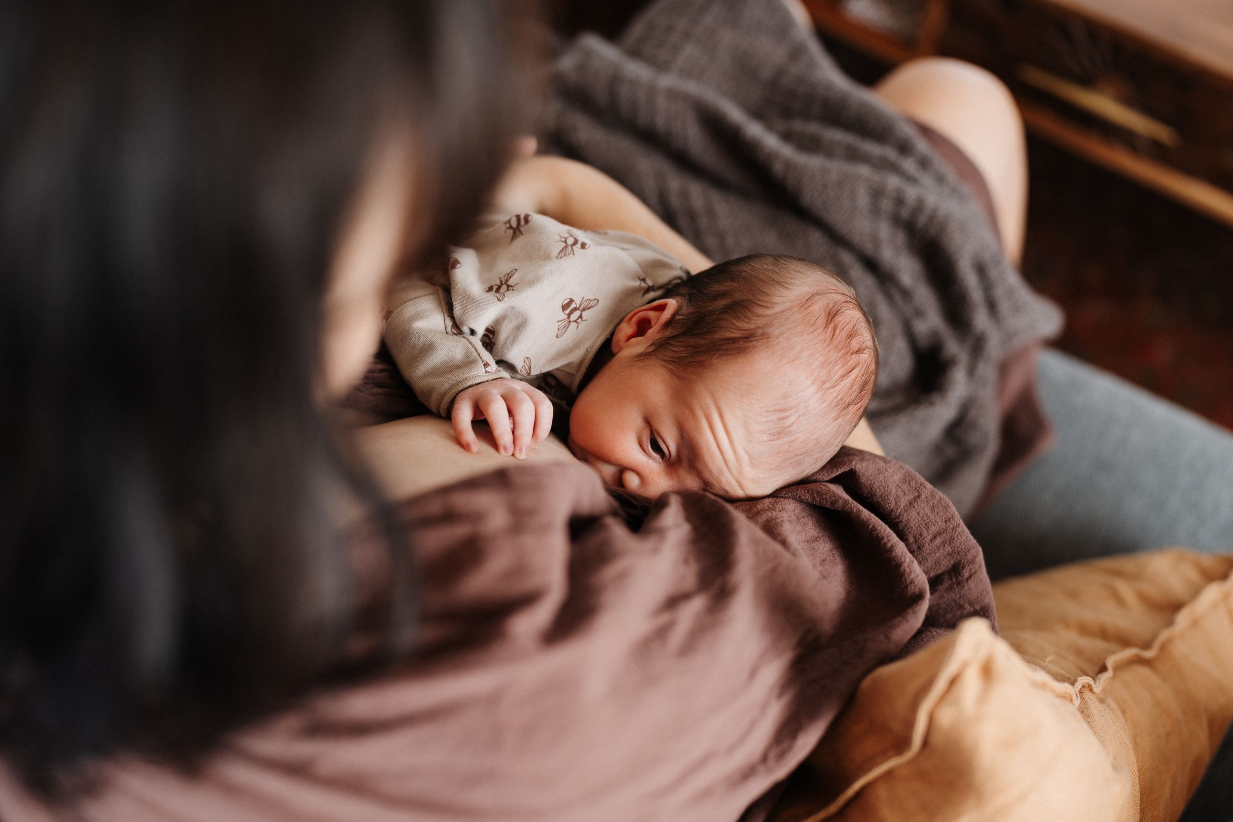 A sleeping baby in brown clothing rests peacefully while being cradled in someone's arms.