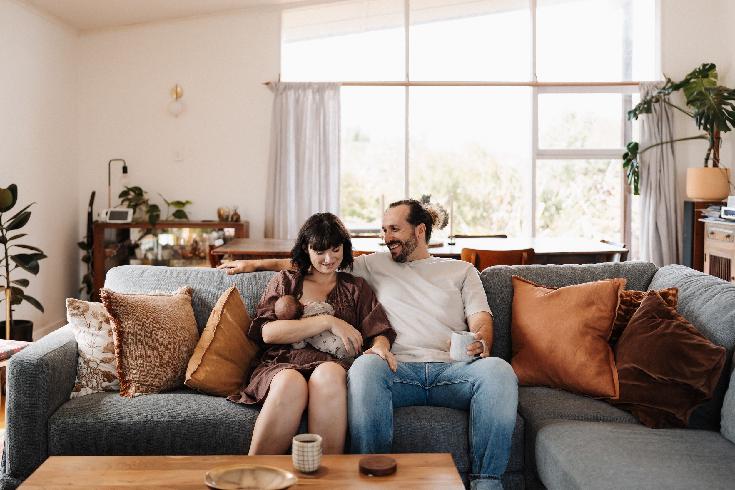 A couple relaxes together on a cozy gray sofa in a bright living room with natural lighting.