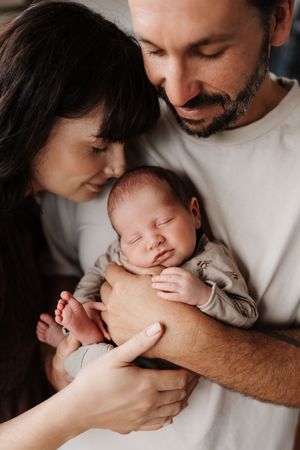 A tender family moment as parents cradle their sleeping newborn baby in a warm embrace.