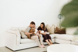A cozy indoor photoshoot shows a couple lounging on a white sofa in casual attire.