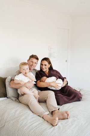 Family cuddles together on a grey striped bed showing tender moments of connection.