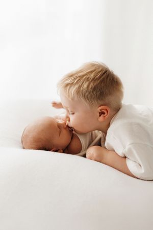A sweet moment between siblings as older child gently kisses newborn on white background.