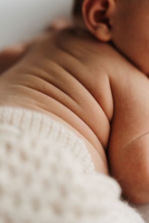 Close up shot of an infant's chubby skin folds and white clothing in soft natural lighting.
