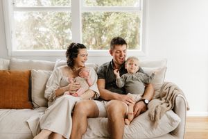 A family relaxes together on a white couch near bright windows in a living room.
