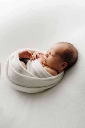 Sleeping newborn wrapped in white swaddle on minimalist background.