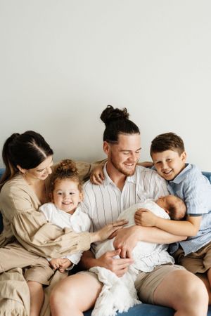 Family of five cuddles together on couch during intimate indoor photo session.